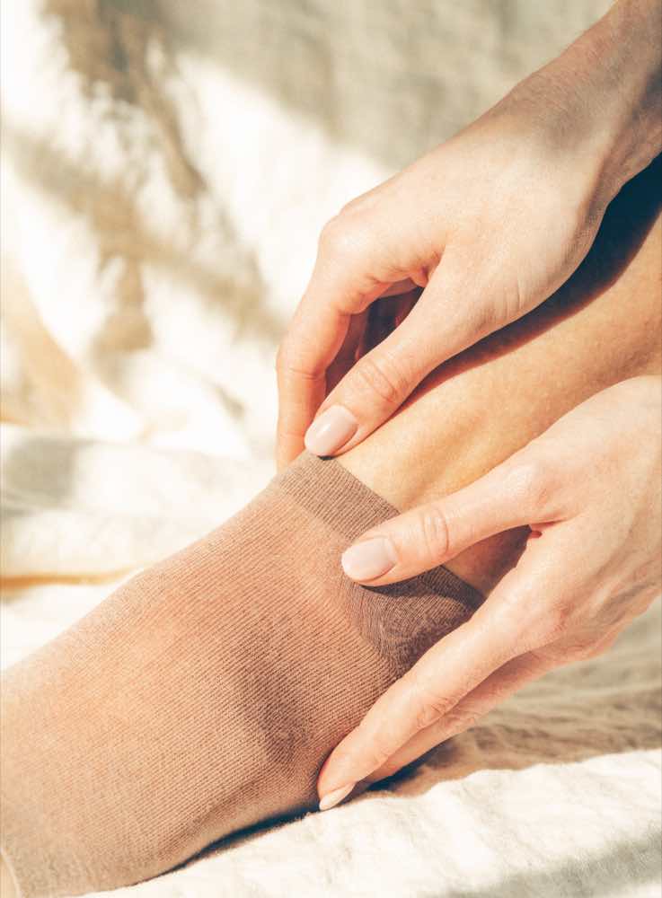 Hands smoothing a nude compression stocking over an ankle